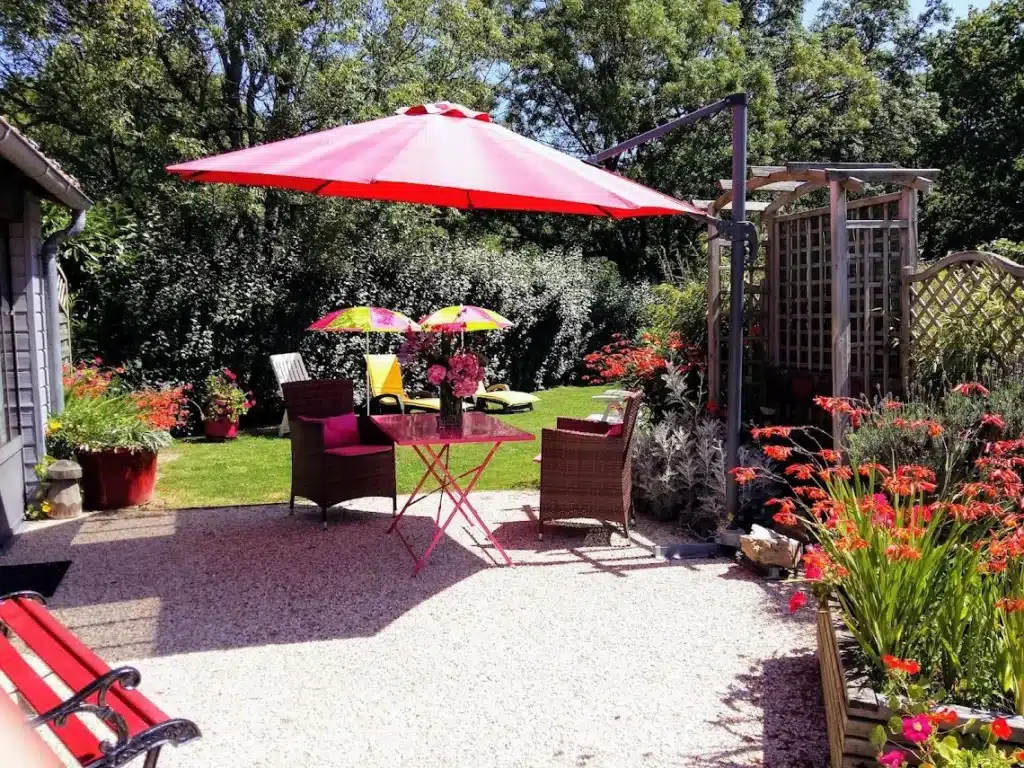 jardin et terrasse du gîte avec plantes vertes, fleurs, tables et chaises ombragées